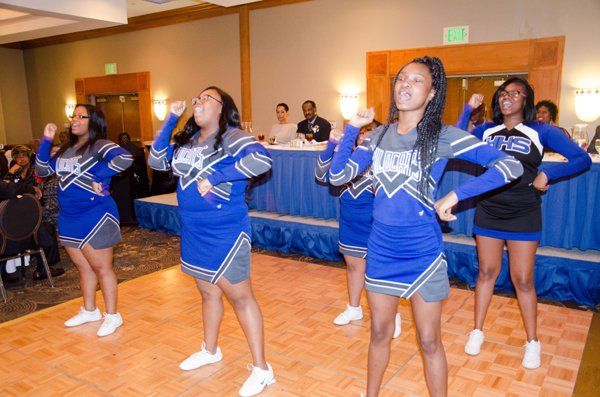 Cheerleaders in blue, gray, and white uniforms perform at an event.