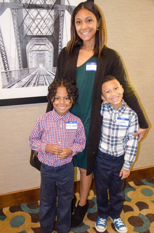 Woman and two young children smiling, indoors; the background includes a framed black and white bridge photo.