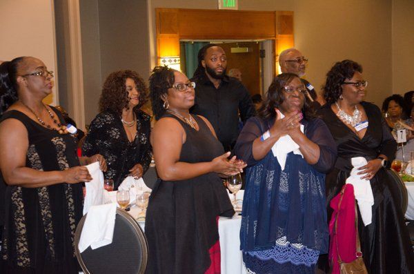 Group of people at a formal event, some clapping and looking forward. Well-dressed in a banquet hall.