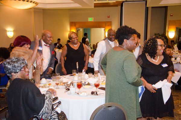 People at a formal event, some standing near a table with food and drinks, celebrating.
