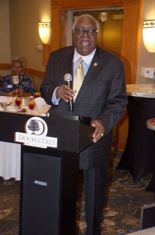 Man in suit speaking at a DoubleTree hotel podium, holding a microphone.