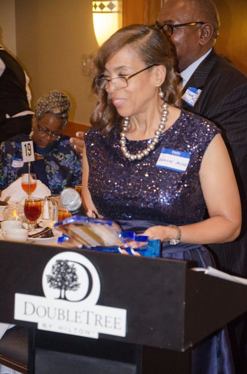 Woman in blue sequin dress at a podium holding an award, DoubleTree logo in foreground.