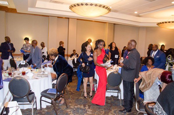 Guests mingle in a banquet hall with round tables set for a formal event.