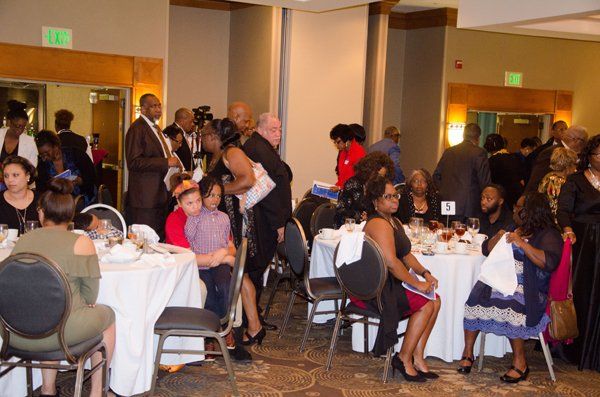 People at tables in a banquet hall, some standing and conversing, others seated.