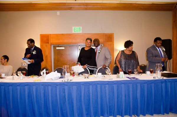 People stand behind a table covered in blue cloth; a reception or event.