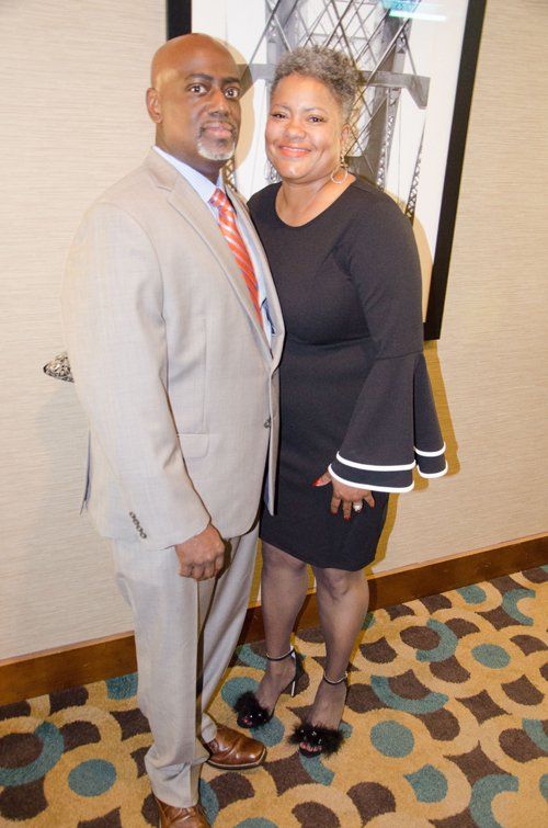 Man in suit and woman in black dress pose together.