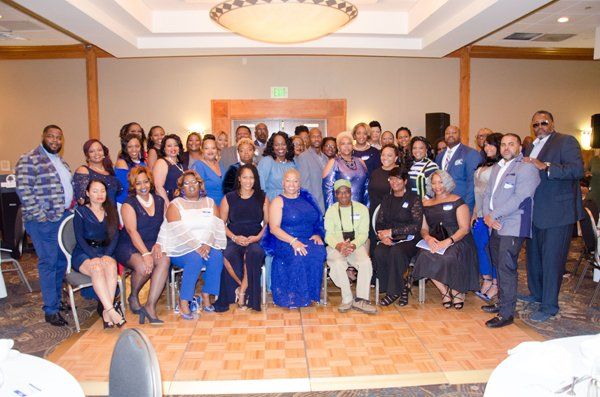 Group of people, mostly in blue attire, pose for a photo in a banquet hall.