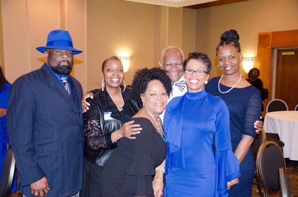 Group of people smiling, posing for a photo at an event; indoor setting with neutral lighting; some wearing blue.