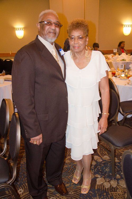 A couple poses at an event, man in a suit, woman in a white dress.