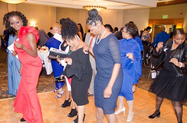 People dancing at an event in a ballroom. Women in dresses of various colors, smiling and moving to music.
