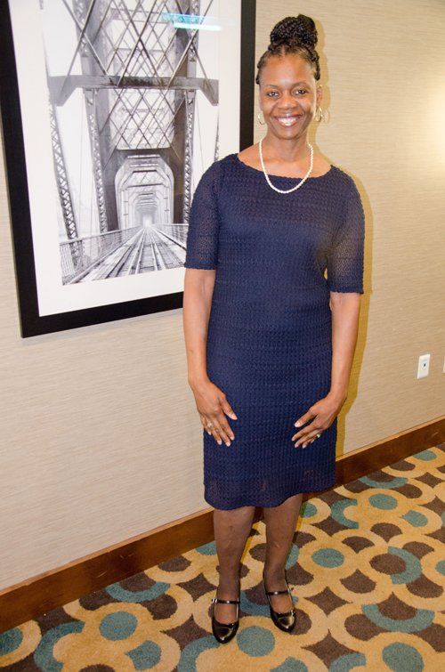 Woman in blue dress stands by a black and white framed photo. She smiles.