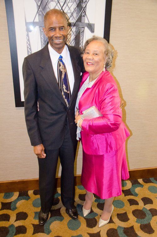 Man in suit and woman in pink suit smiling, posing indoors.