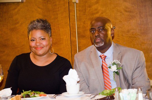 Couple seated at a table; woman in black top smiles, man in suit looks forward.