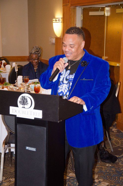 Man in blue jacket speaks at a podium at a DoubleTree event.