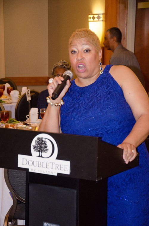 Woman speaking at a DoubleTree podium, wearing a blue dress.