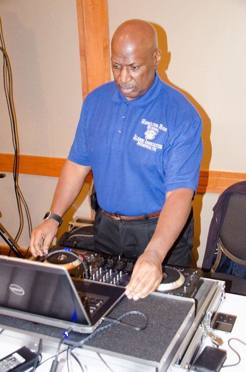 Man in blue shirt mixing music on a DJ setup, laptop open, indoors.