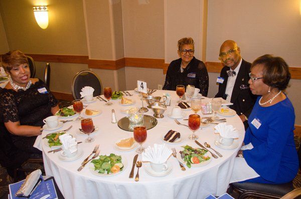 Four people seated around a round table set for a meal. The group appears to be in a restaurant or event space.