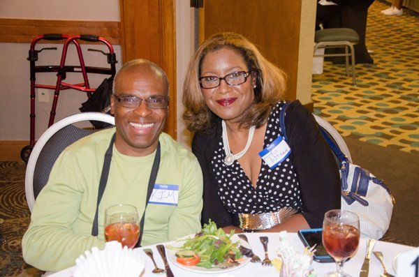 Two smiling people seated at a table, enjoying a meal; glasses of iced tea are present.