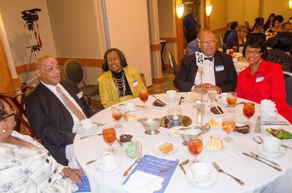 People seated around a table at an event, some smiling, with food and drinks.