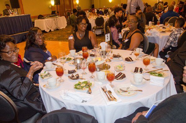People seated at a round table, eating and conversing at a banquet. Various dishes and drinks visible.