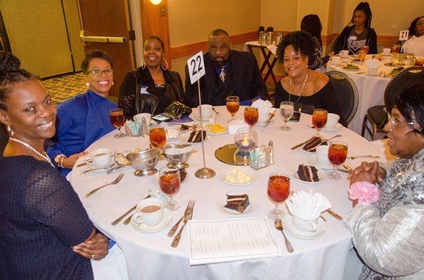 People seated at a round table, celebrating. The table has food, drinks, and a centerpiece.