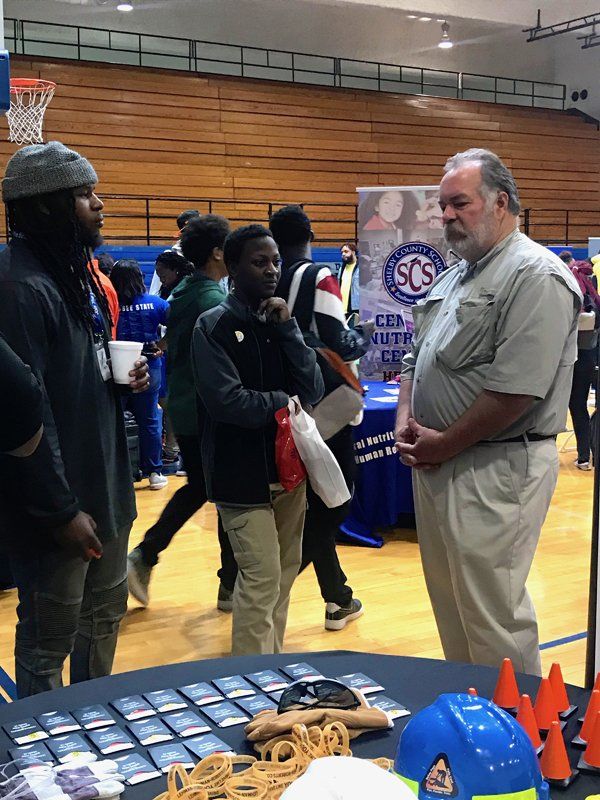 People at an informational booth, possibly a school or career fair, indoors.
