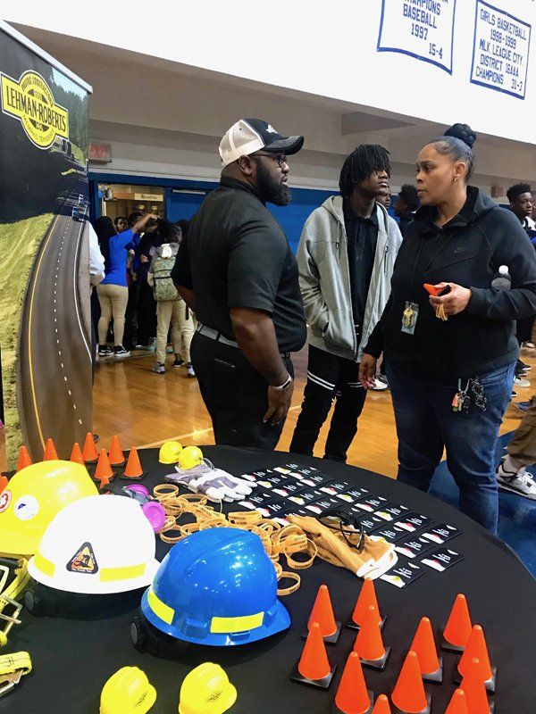 People at a table with construction-themed items. A banner is in the background.