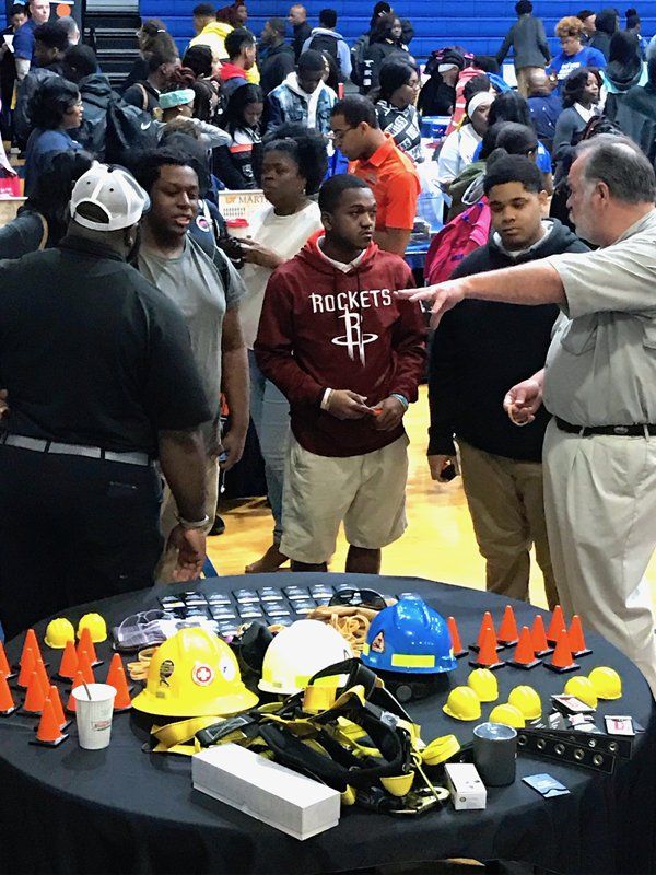 People at a table with equipment and construction hats; one man points.