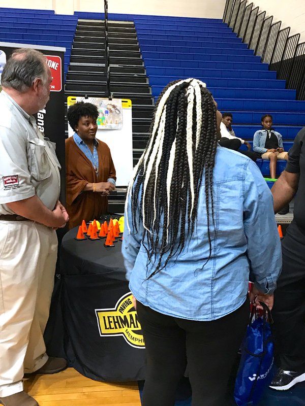 People at a Lehman College event. A woman with braided hair faces a booth, others stand near by.