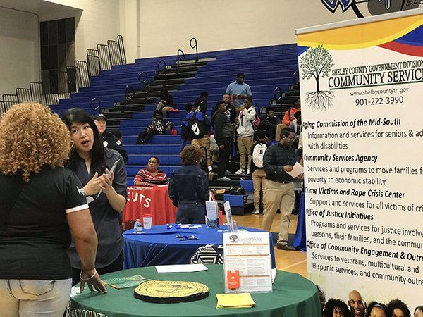 People at a community services event, with a display, inside a gymnasium.