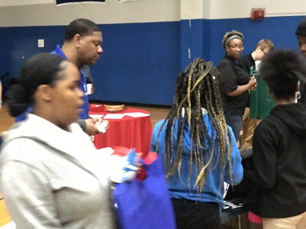 People at a table, some are looking at papers and others are holding bags. In a gymnasium with blue walls.