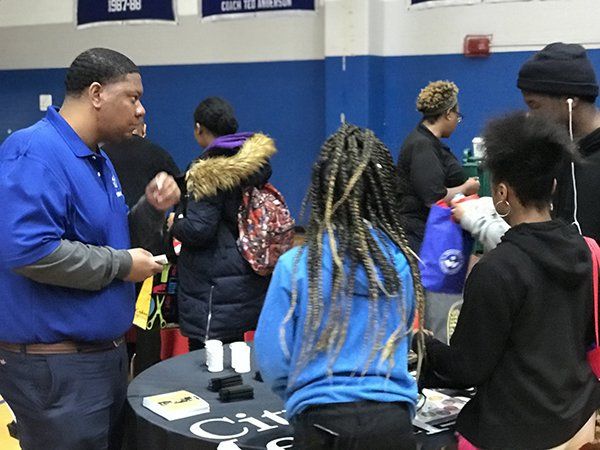 People at a table. A man in blue shirt talks to people. Indoor setting with blue wall.