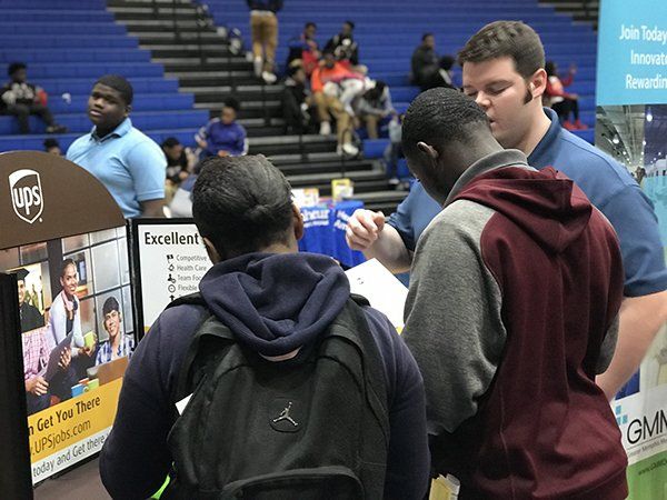 People at a job fair looking at a UPS booth; indoors.
