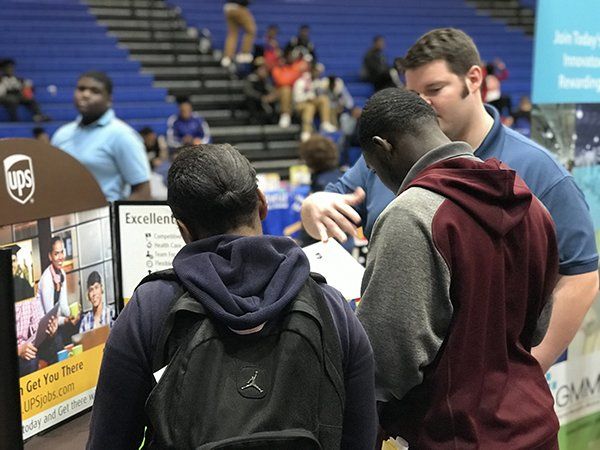 Two people looking at a UPS booth, possibly at a job fair in a gymnasium.