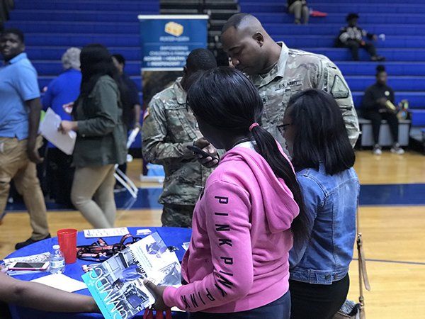People at a table, looking at materials, likely at a career fair in a gymnasium.