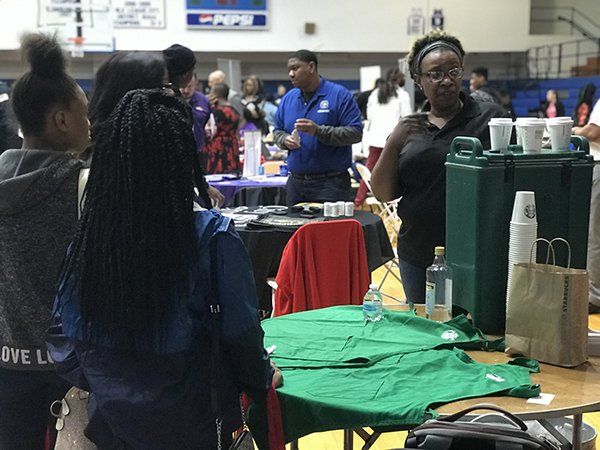 People at a table with promotional items and drinks in a gym; event.