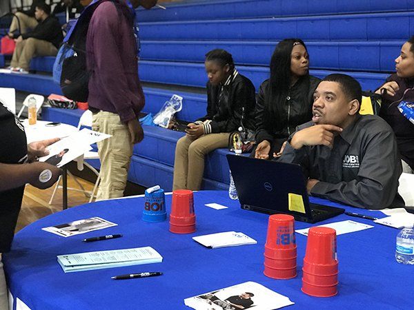 People at a table with brochures and a laptop, discussing information in a gym.
