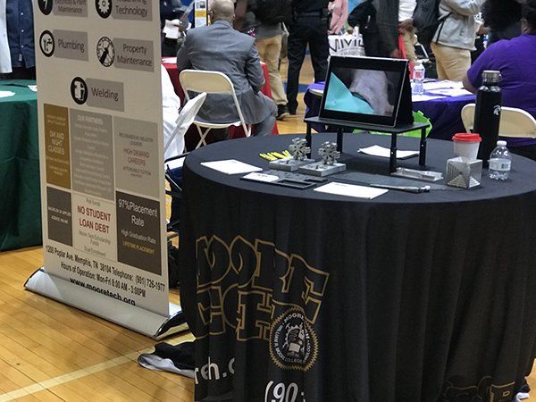 Booth at a career fair with services banner, table, and a display screen showing plumbing work.