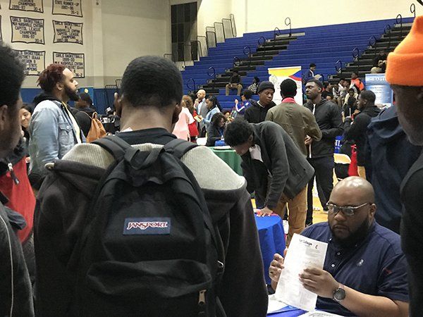 Students at a career fair in a gymnasium looking at information at tables and networking.