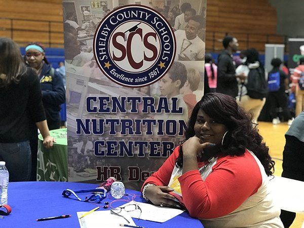 Woman at a booth for Shelby County Schools Central Nutrition Center. Blue table, banner, event.