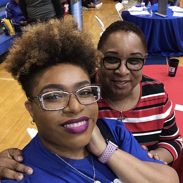 Two women smiling, posing for a selfie in a gymnasium.