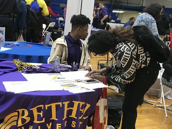 A person signing a form at a Bethel University table. Student and advisor interaction. Indoor event.