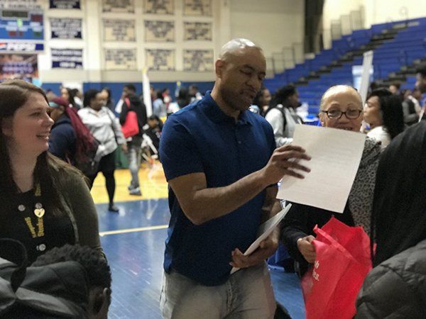 Man in blue shirt reviews papers in a crowded gymnasium.