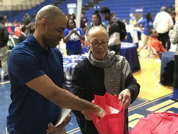 Man and woman looking into a red bag at a school event. They are standing in a gymnasium.