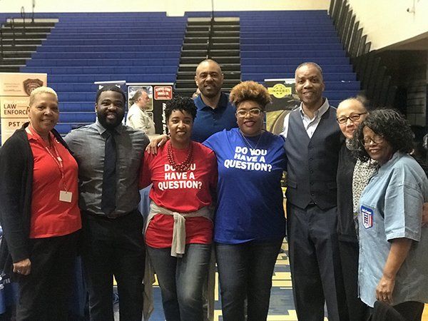 Group of people smiling, posing for a photo at an indoor event with blue bleachers.