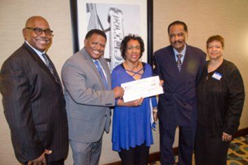 Five people at an event; a person in a blue top is handed a check.