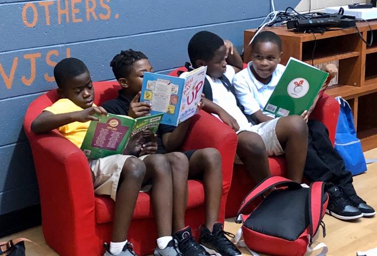 Four young boys reading books together in a red armchair.