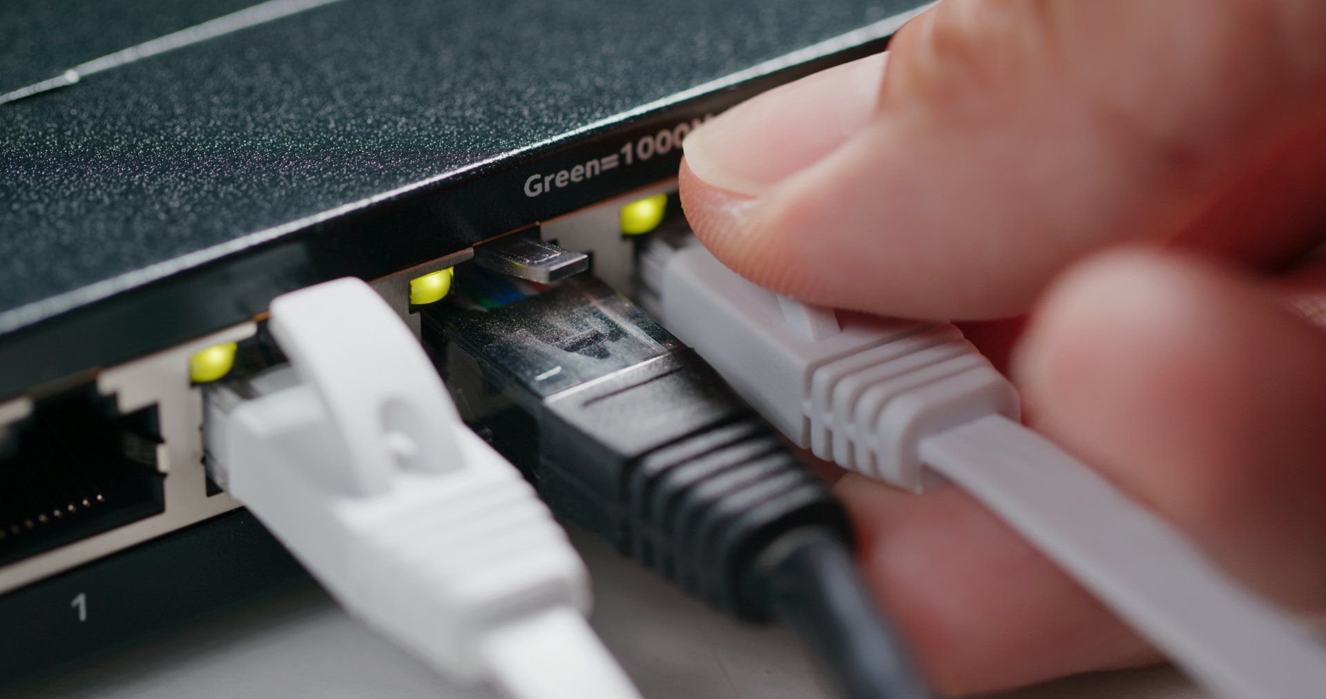 Hand plugging a gray Ethernet cable into a network switch with green status lights