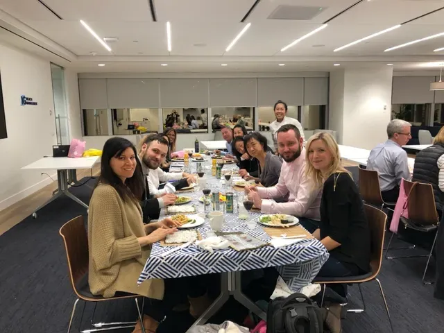 People seated around a table, eating. The table has a blue and white checkered tablecloth. Brightly lit room.