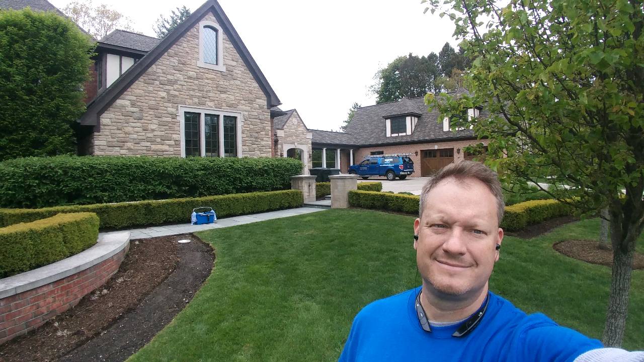 A man in a blue shirt is standing in front of a house. Devine Shine Window Cleaning Canton MI.